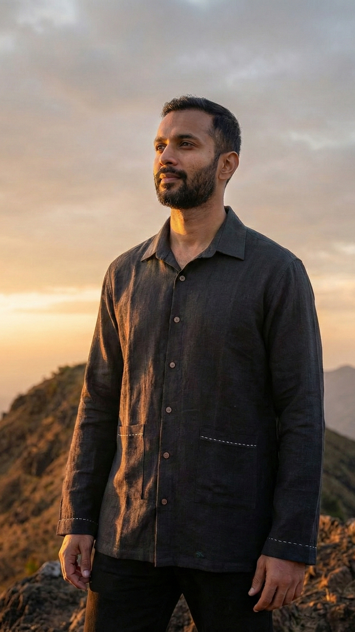 Man standing on a mountain wearing a black shirt with embroidery and sunset or sunrise in the background