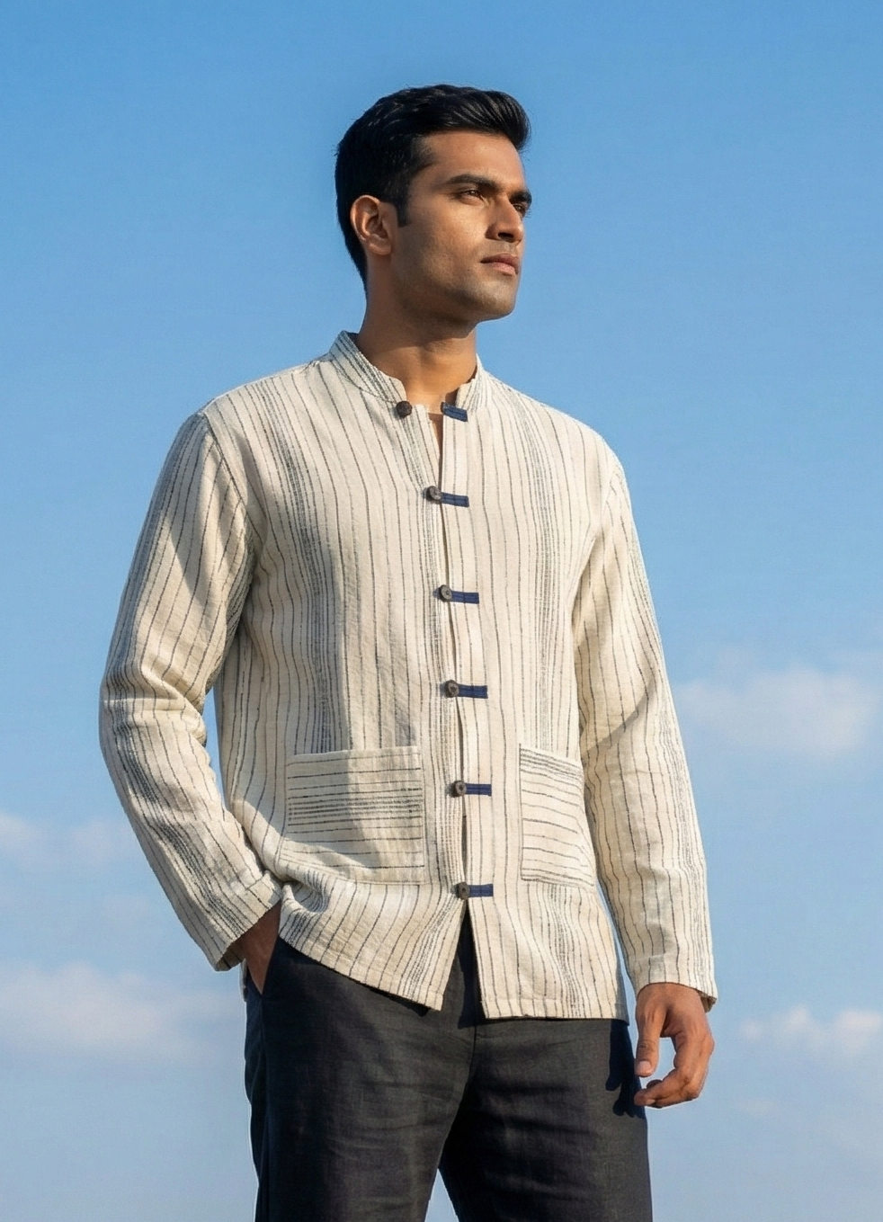 Man wearing a light-colored traditional shirt with black buttons against a blue sky.