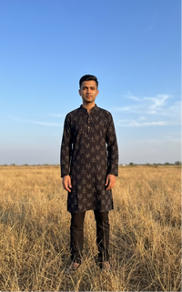 Man in a black ikat kurta standing in a field with a clear blue sky