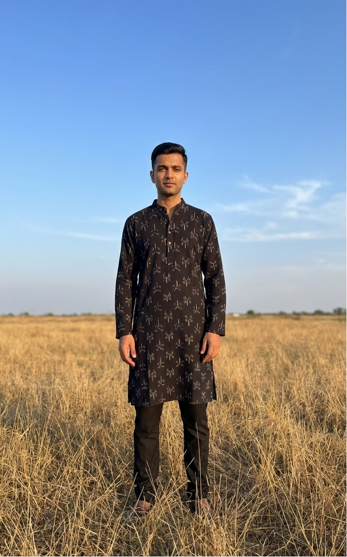 Man in a black ikat kurta standing in a field with a clear blue sky