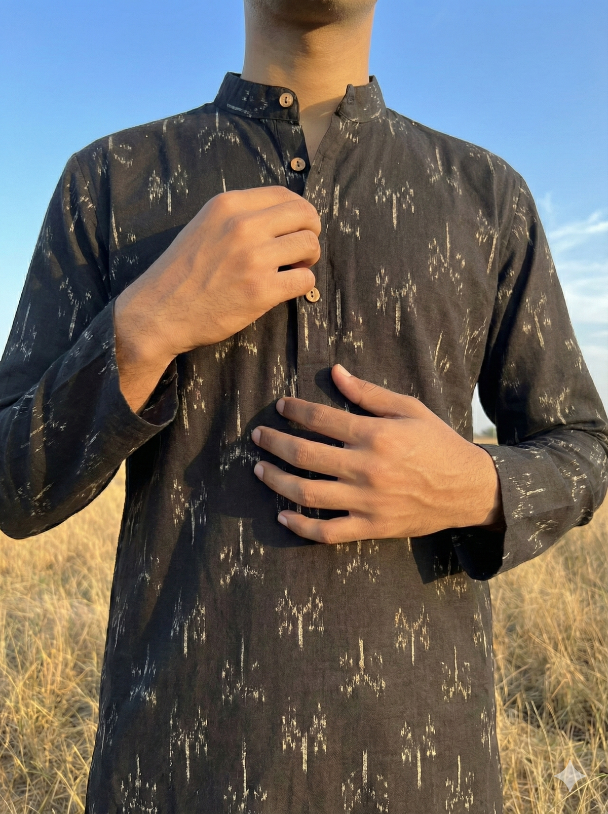 Person wearing a black ikat kurta in an outdoor setting with a clear sky.