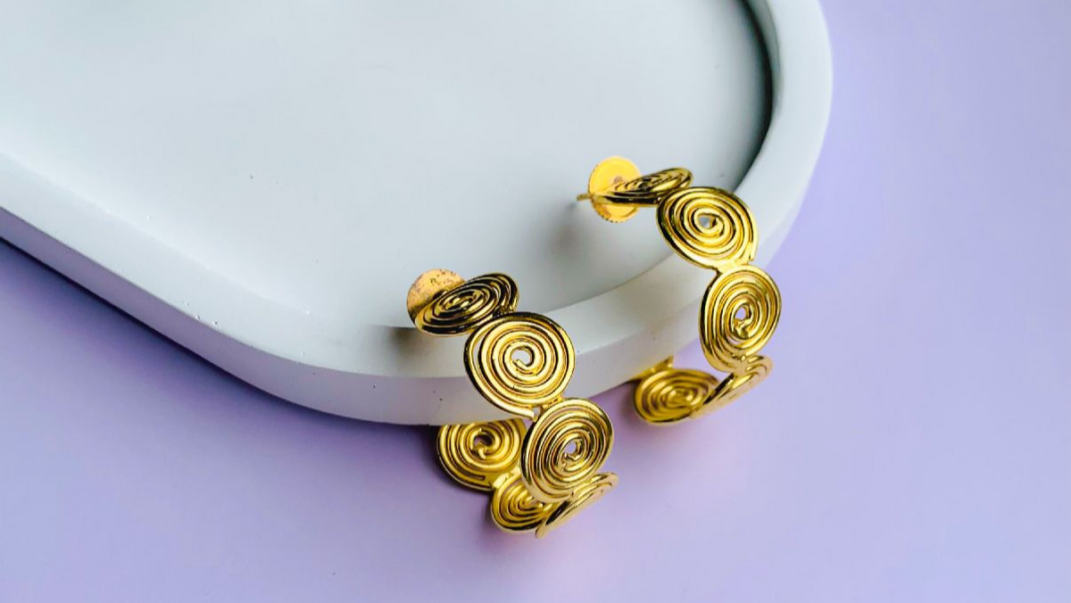 Gold spiral earrings on a white dish with a light purple background