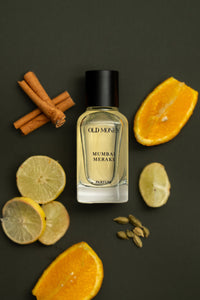 Perfume bottle labeled 'Old Money' surrounded by citrus fruits and spices on a dark surface